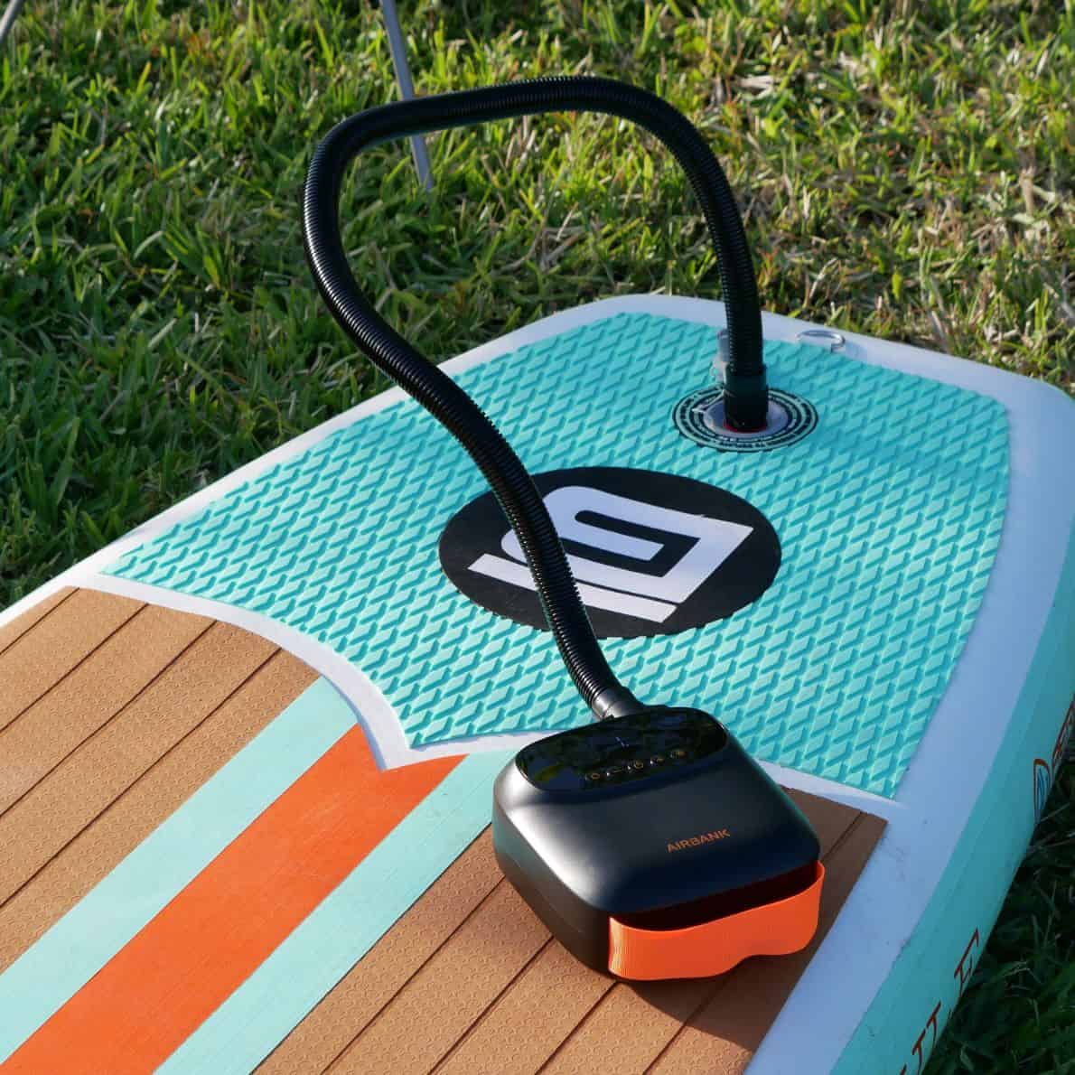 lectric pump inflating a turquoise and wood-patterned paddleboard on grass.