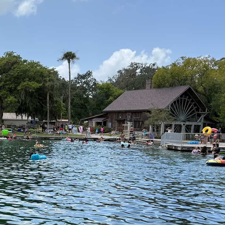 Crowded swim area at De Leon Springs State Park with people floating near a historic mill building.
