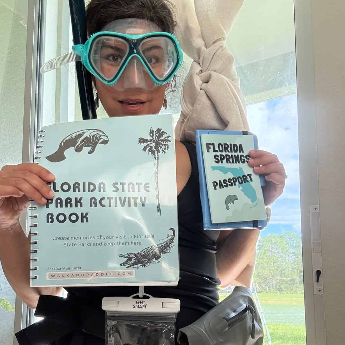 Woman wearing snorkel gear holding a Florida State Park Activity Book and a Florida Springs Passport.