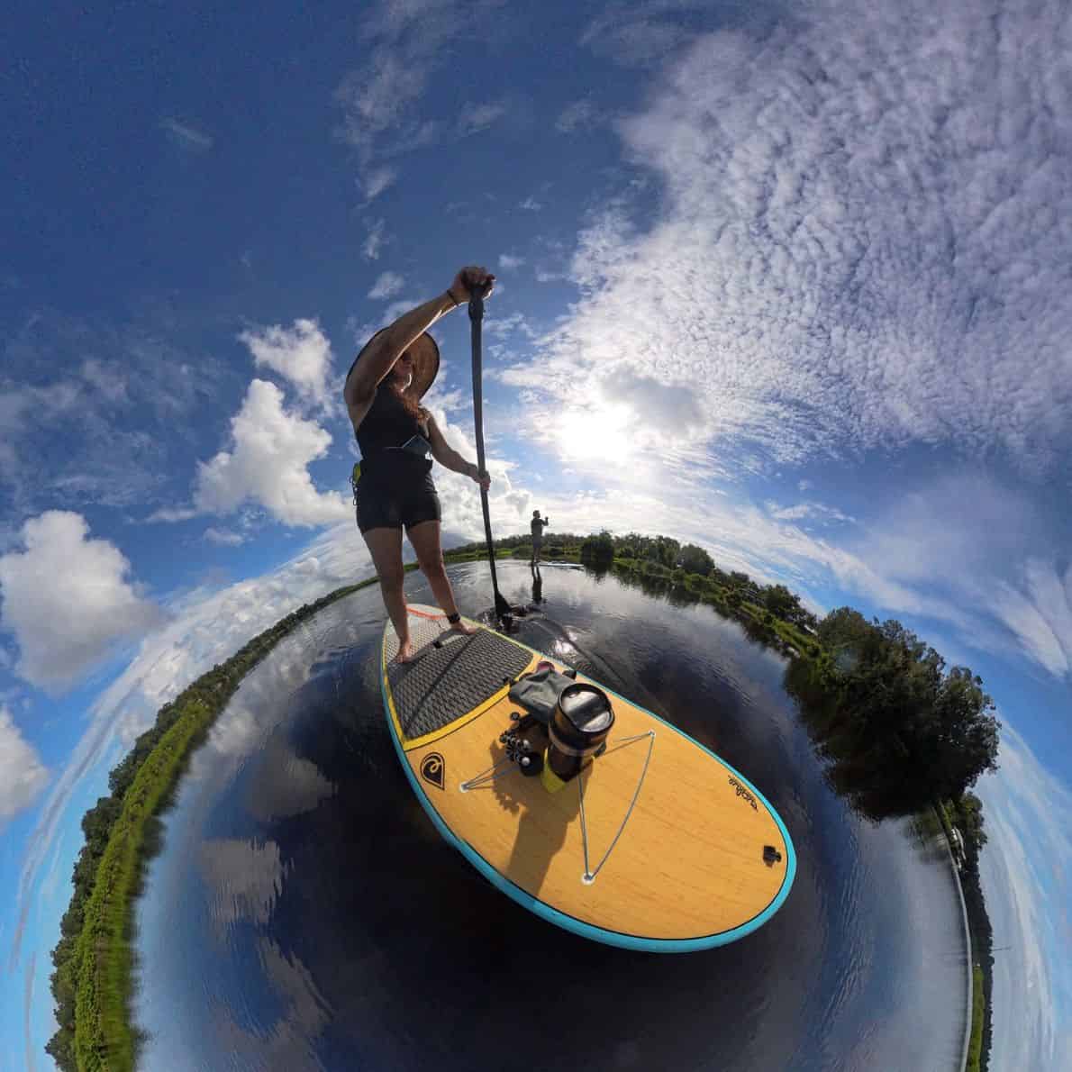 Woman paddleboarding on calm water under a partly cloudy sky at Doris Leeper Spruce Creek Preserve.