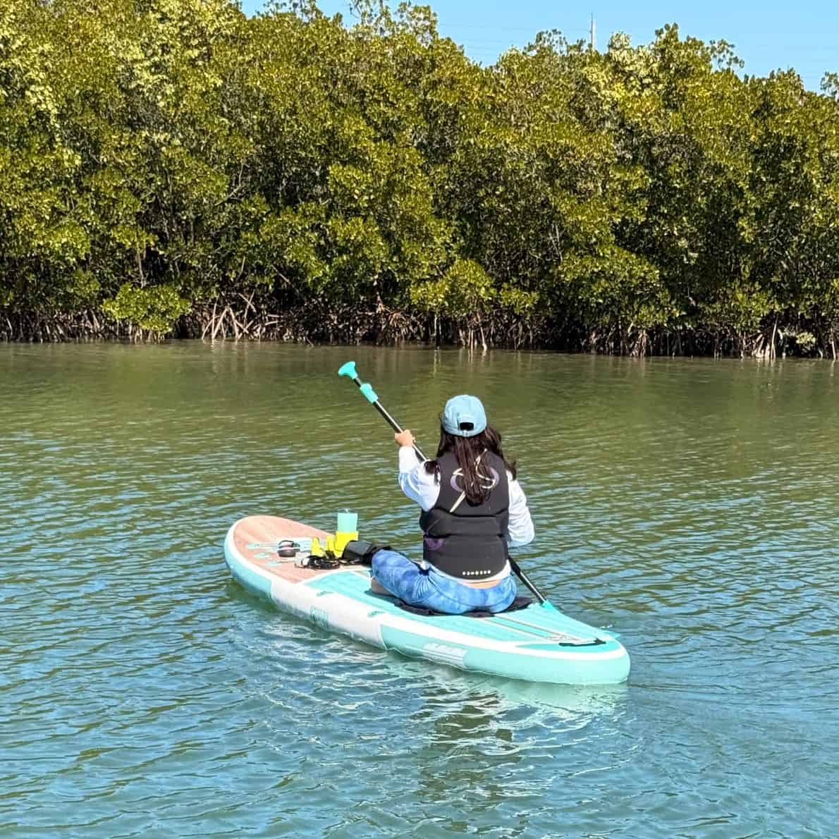 Woman paddling away on a teal Niphean paddleboard at Callalisa Creek, mangroves lining the shore in New Smyrna Beach.