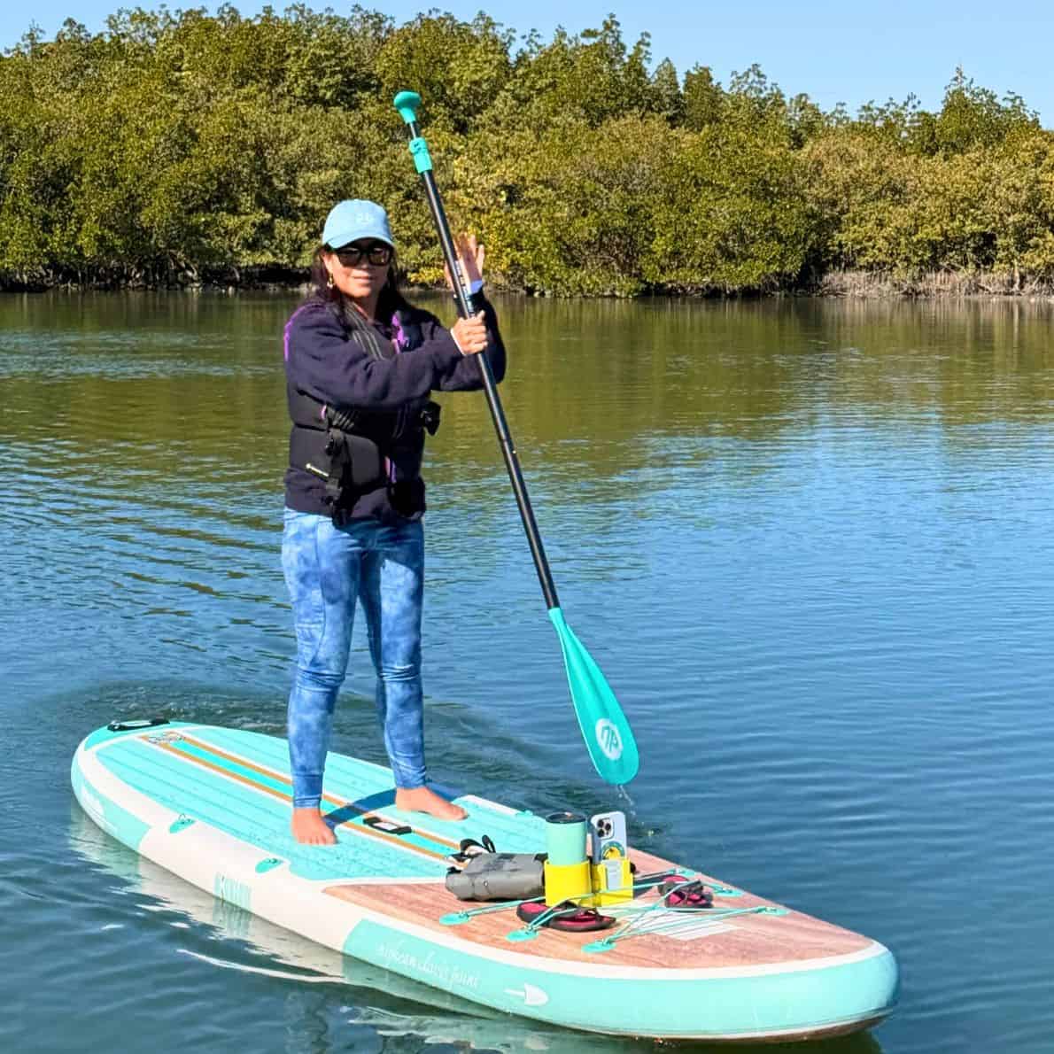 Woman standing barefoot on a teal Niphean paddleboard at Callalisa Creek with mangroves behind her.