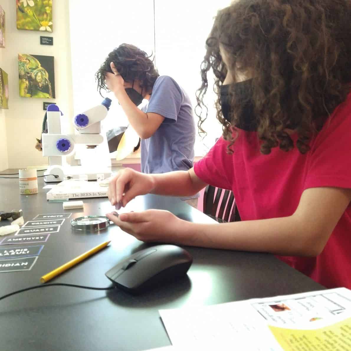 Two kids using microscopes to examine rocks at a museum table