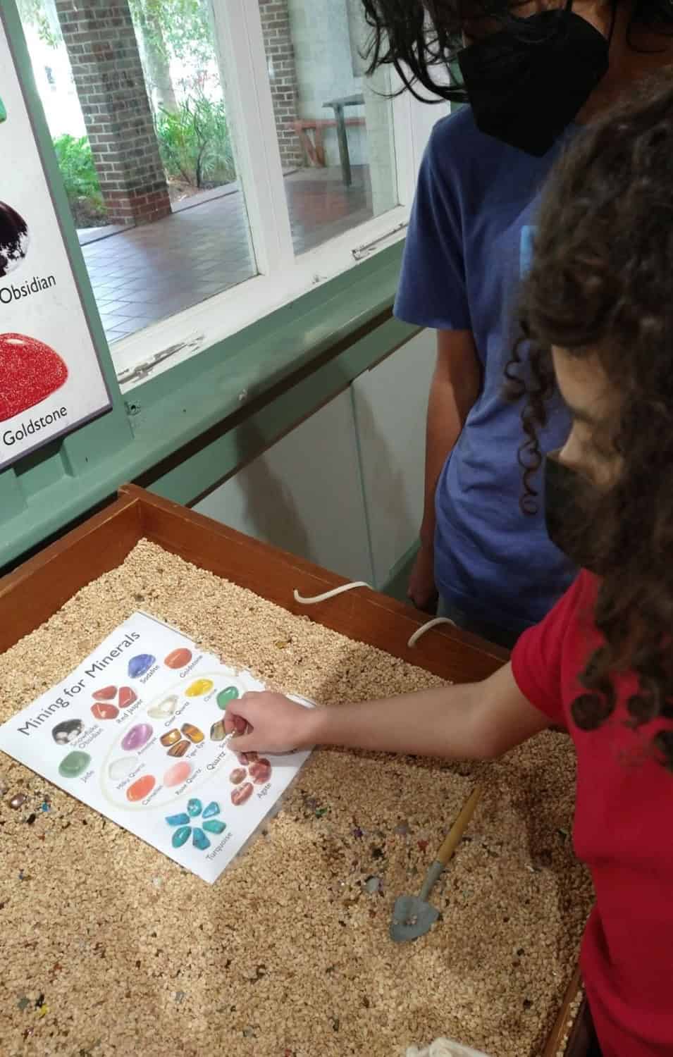 Two kids digging through a sand bin while matching stones to a mineral chart