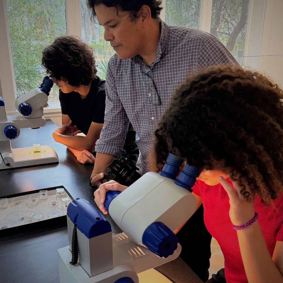 Adult and two teens using microscopes to examine samples at a museum table