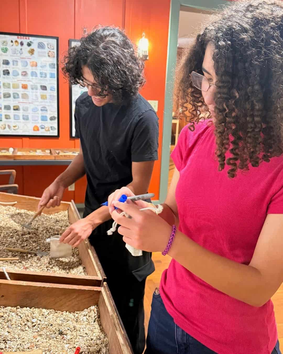 Two teens digging through gravel bins to find minerals in an indoor exhibit
