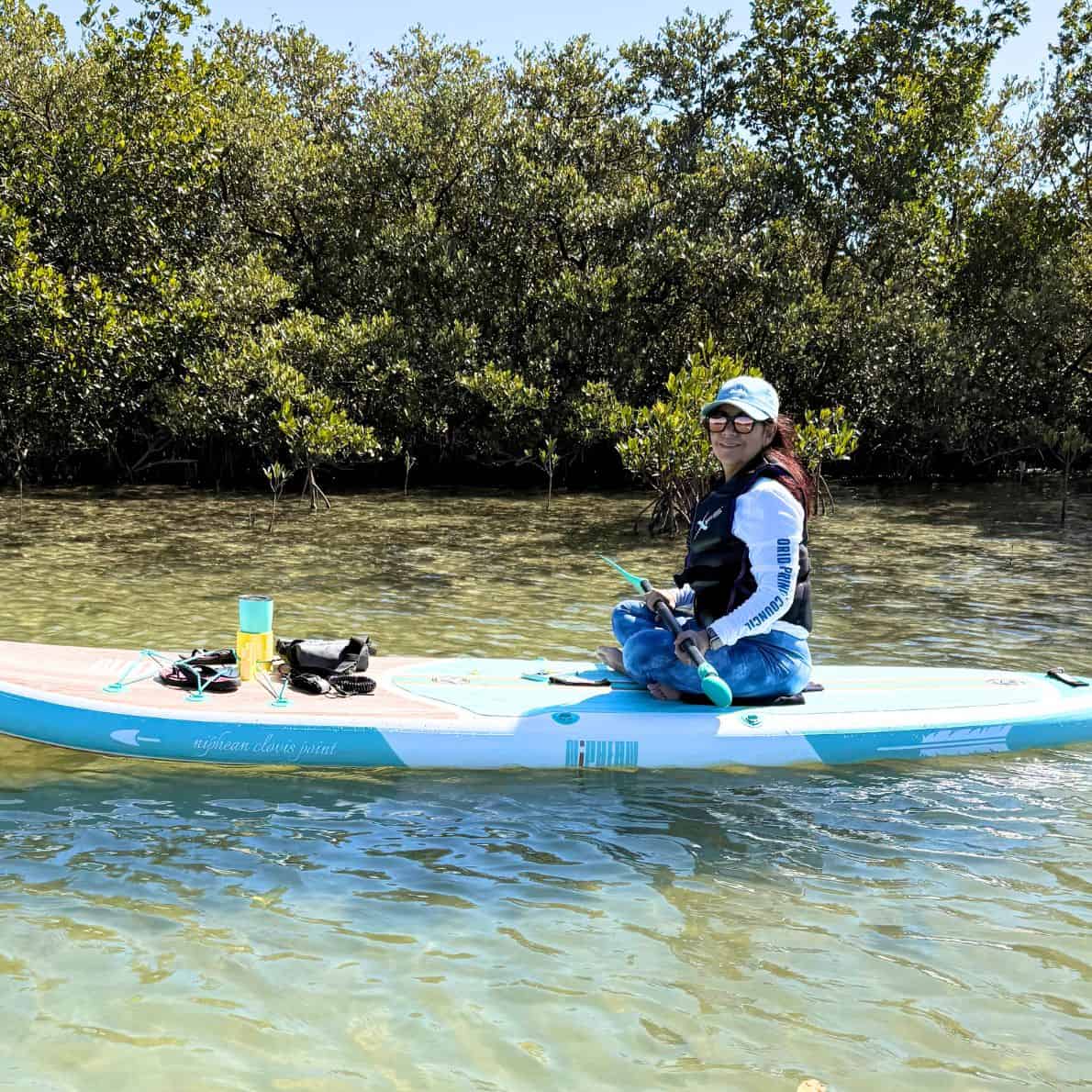 Woman sitting on a paddleboard in the shallow waters of Callalisa Creek surrounded by mangroves.