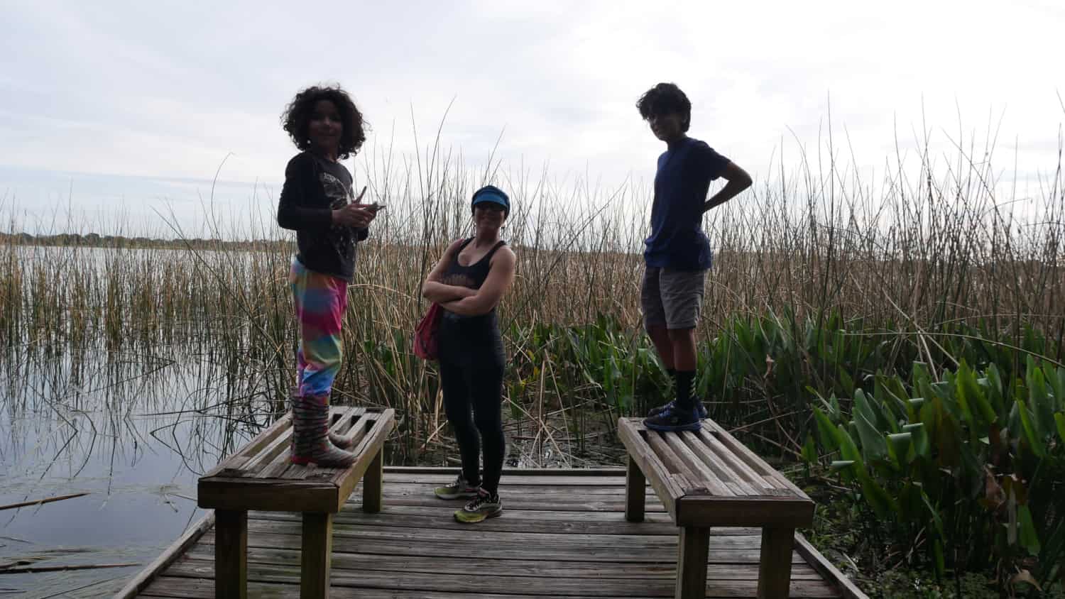 Woman and two children standing on a wooden platform overlooking a marsh and lake.