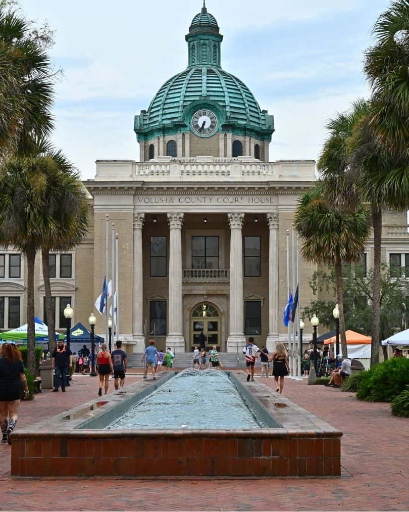 Historic Volusia County Courthouse with a fountain and people gathered in downtown DeLand.
